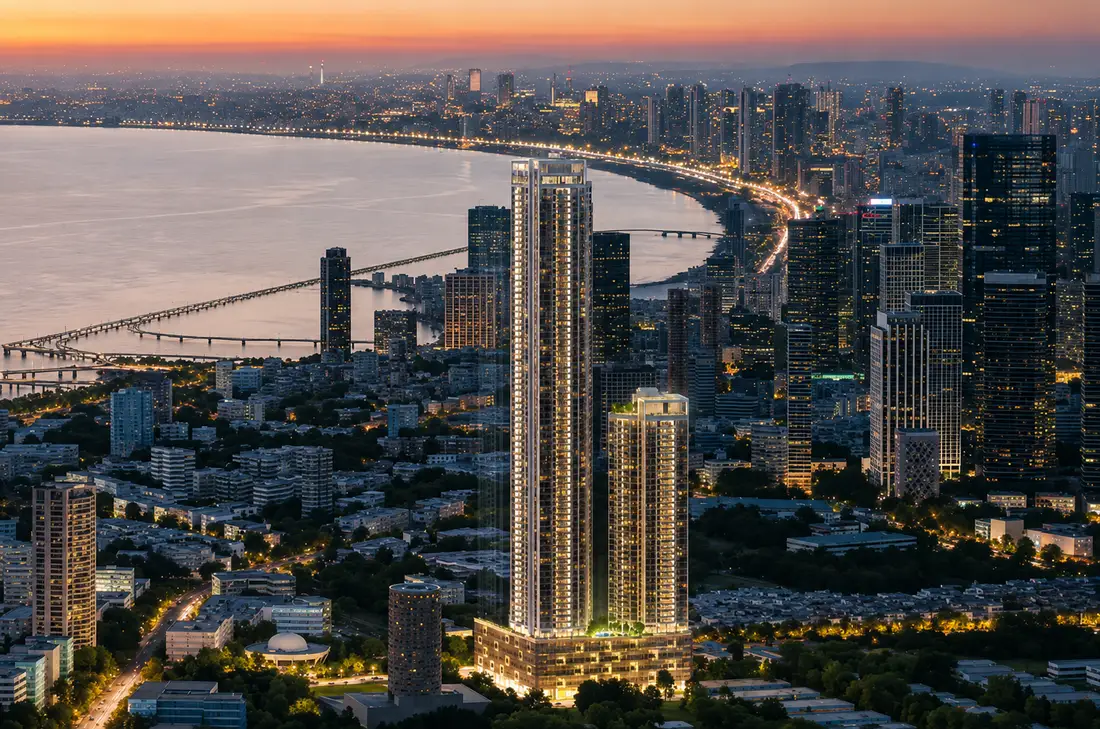 Wide aerial of Godrej Trilogy after sunset, showing the bay, the sea bridge, and the lit South Mumbai skyline